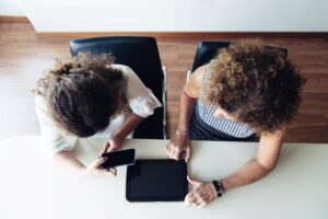 Overhead shot of two women conversing over a phone and a tablet